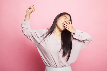 Sleepy young Asian woman yawn on pink backgroundの写真素材