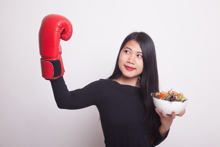 Young Asian woman with boxing glove and salad on white backgroundの写真素材