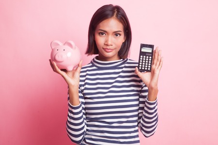 Asian woman with calculator and piggy bank on pink backgroundの写真素材