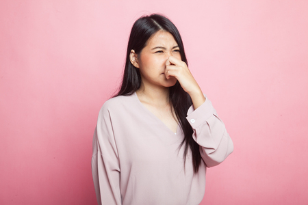 Young Asian woman  holding her nose because of a bad smell on pink backgroundの写真素材