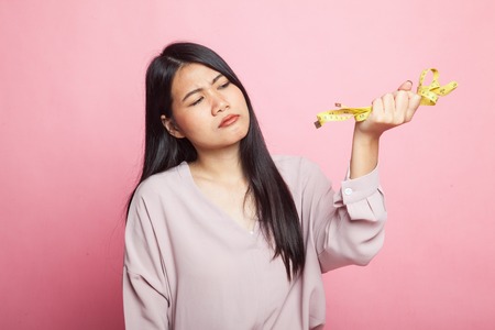 Unhappy young Asian woman with measuring tape on pink backgroundの写真素材