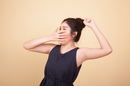 Sleepy young Asian woman yawn  on beige backgroundの写真素材