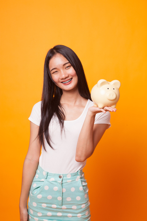 Young Asian woman with a pig coin bank on bright yellow backgroundの写真素材