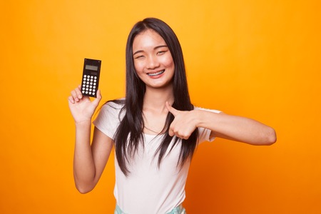 Asian woman thumbs up with calculator on bright yellow background