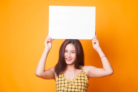 Young Asian woman with white blank sign on yellow backgroundの写真素材