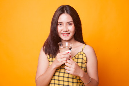 Young Asian woman with a glass of drinking water on yellow backgroundの写真素材