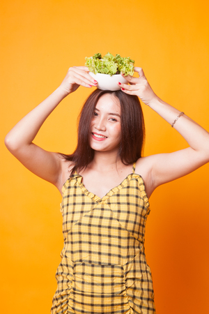 Healthy Asian woman with salad on yellow backgroundの写真素材