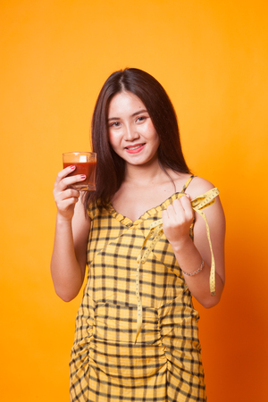 Young Asian woman with tomato juice and measuring tape on yellow backgroundの写真素材