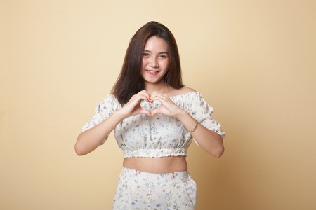 Young Asian woman show heart hand sign on beige backgroundの写真素材