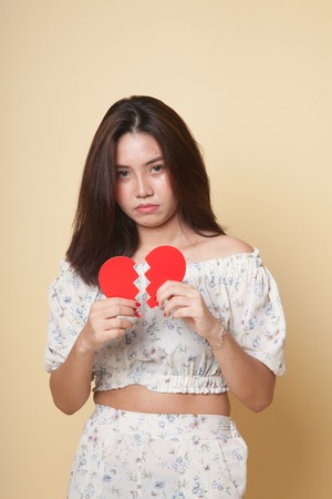 Beautiful young Asian woman with broken heart on beige backgroundの写真素材