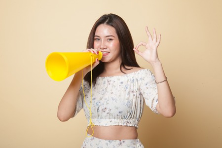 Beautiful young Asian woman show OK  announce with megaphone on beige background
