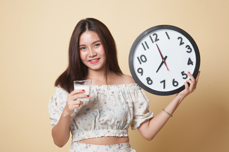 Healthy Asian woman drinking  glass of milk hold clock on beige backgroundの写真素材