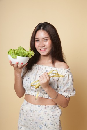 Healthy  Asian woman with measuring tape and salad on beige backgroundの写真素材