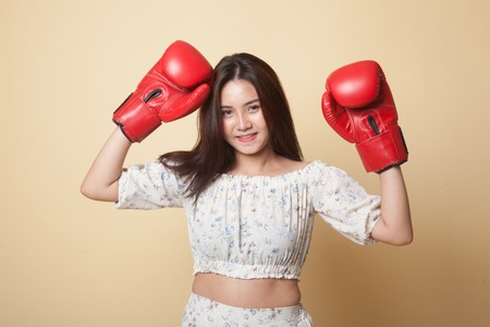 Young Asian woman with red boxing gloves on beige backgroundの写真素材