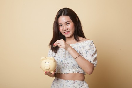 Asian woman with coin and pig coin bank on beige backgroundの写真素材