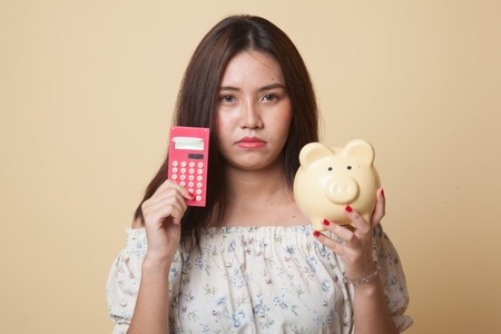 Unhappy Asian woman with calculator and piggy bank on beige backgroundの写真素材