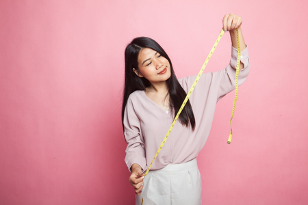 Young Asian woman with measuring tape on pink backgroundの写真素材