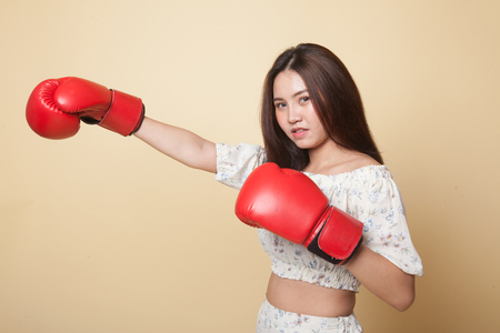 Young Asian woman with red boxing gloves on beige backgroundの写真素材