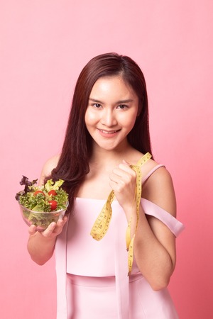 Unhappy Asian woman with measuring tape and salad on pink backgroundの写真素材