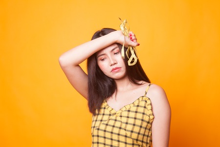 Unhappy young Asian woman with measuring tape on yellow background