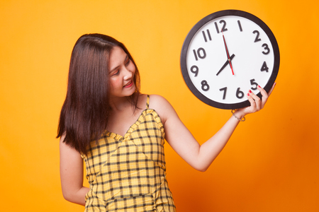 Young Asian woman with a clock on yellow backgroundの写真素材
