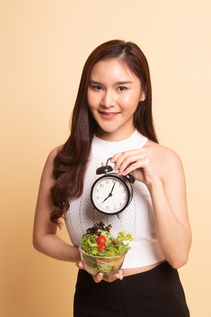 Young Asian woman with clock and salad   on beige background.の写真素材