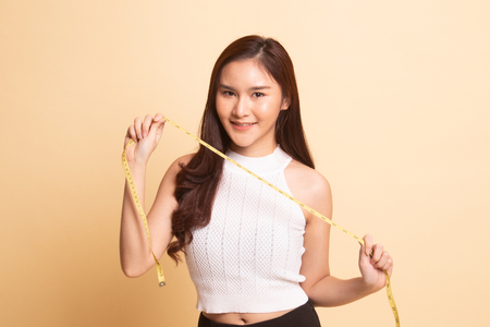 Young Asian woman with measuring tape   on beige background.の写真素材
