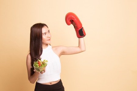 Young Asian woman with boxing glove and salad   on beige background.の写真素材