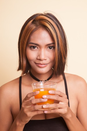 Young Asian woman drink orange juice on beige backgroundの写真素材