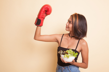 Young Asian woman with boxing glove and salad on beige backgroundの写真素材
