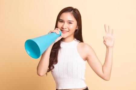 Beautiful young Asian woman show OK  announce with megaphone   on beige backgroundの写真素材