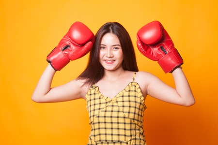 Young Asian woman with red boxing gloves on yellow background