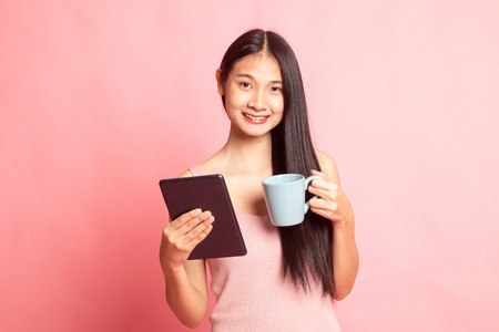 Young Asian woman with a computer tablet and coffee on pink background