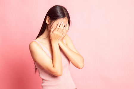Sad young Asian  woman cry with palm to face on pink backgroundの写真素材
