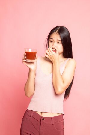 Young Asian woman hate tomato juice on pink backgroundの写真素材
