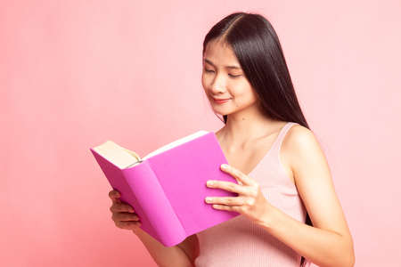 Young Asian woman read a book on pink backgroundの写真素材