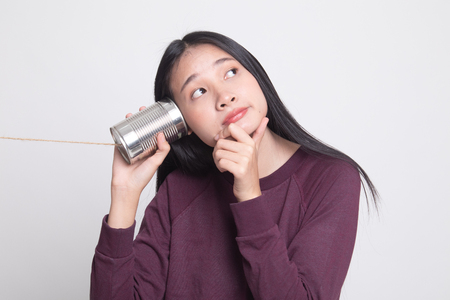 Young Asian woman hearing with tin can phone and thinking on white backgroundの写真素材