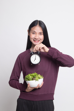 Young Asian woman with clock and salad on white backgroundの写真素材