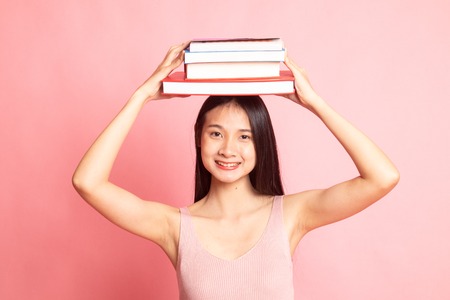 Young Asian woman studying  with may books on pink background