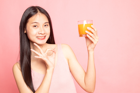 Young Asian woman show OK drink orange juice on pink backgroundの写真素材