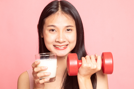 Healthy Asian woman drinking a glass of milk and dumbbell on pink backgroundの写真素材