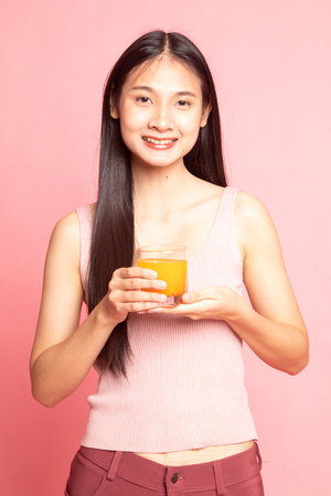 Young Asian woman drink orange juice on pink backgroundの写真素材