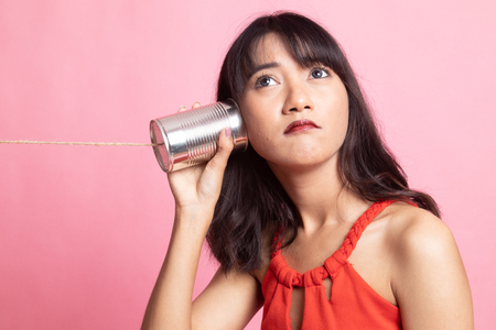 Young Asian woman with tin can phone on pink backgroundの写真素材