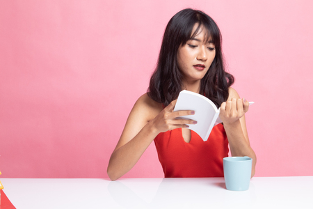 Young Asian woman read a book with cup of coffee on pink backgroundの写真素材