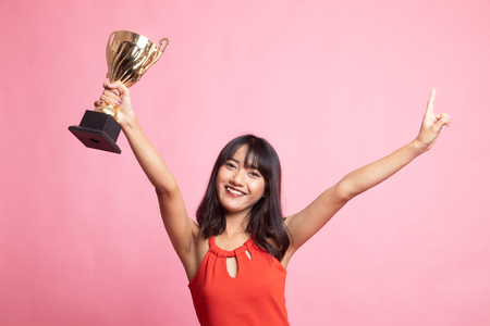 Successful number one winner young asian woman holding a trophy on pink backgroundの写真素材
