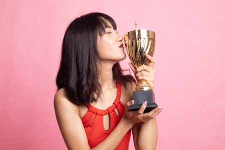Successful young asian woman holding kissing a trophy on pink backgroundの写真素材
