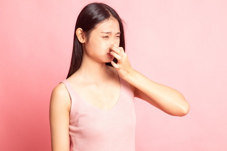 Young Asian woman  holding her nose because of a bad smell on pink backgroundの写真素材
