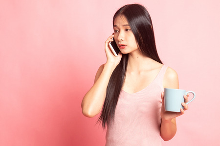 Young Asian woman with mobile phone and coffee cup on pink backgroundの写真素材