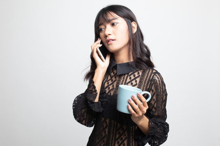 Young Asian woman with mobile phone and coffee cup on white backgroundの写真素材