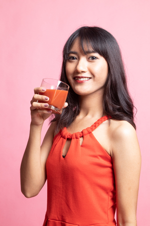 Young Asian woman drink tomato juice on pink backgroundの写真素材